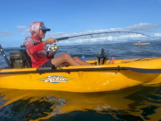 Person fishing with a rod from a yellow Hobie kayak on calm ocean water