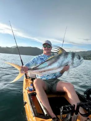 A man sitting in a kayak holds up a large roosterfish on open water