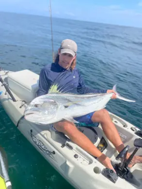 A man sitting in a fishing kayak on the ocean holding a large roosterfish
